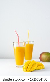 Mango juice in glasses with juice and a straw on a white background, chopped mango and whole, delicious healthy sweet natural drink