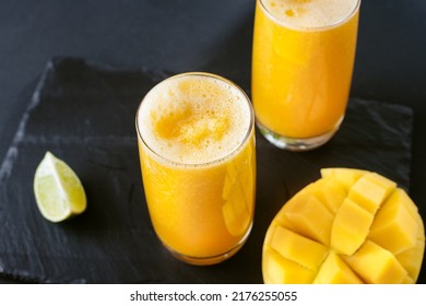 Mango and lime juice nectar. A refreshing summer drink on a black background. Bright yellow and black colors. Mango juice on a dark background. Summer drink with ice and slices of mango and lime.