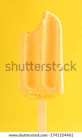 mango pudding flavor popsicle with a bite on a yellow background