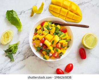 Mango Salsa Salad Bowl With Fresh Tomato And Lime On A White Marble Table In Top View.