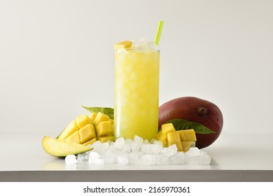 Mango Slush Drink In Tall Glass With Fruit And Crushed Ice Around It On White Table With Isolated Background. Front View. Horizontal Composition.