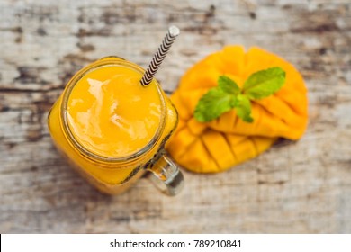 Mango smoothie in a glass Mason jar and mango on a green background. Mango shake. Tropical fruit concept.
