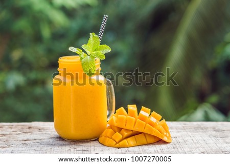 Mango smoothie in a glass Mason jar and mango on a green background. Mango shake. Tropical fruit concept.