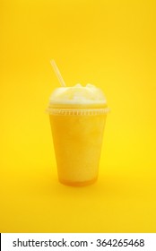 Mango Smoothie on yellow background, served in plastic cup and a straw