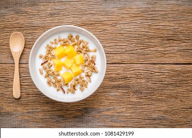 Mango yogurt mixed with whole grains, healthy menu in white bowl, And wooden spoon on wooden background.
