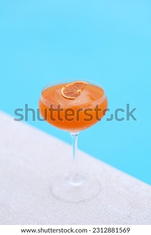 A mango-flavored cocktail in a glass with an orange hue on white and blue background