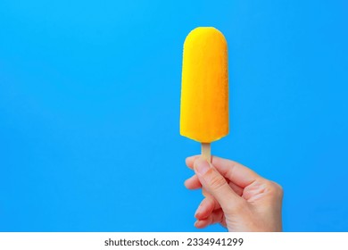 mango-flavored popsicle in a woman's hand on a blue background