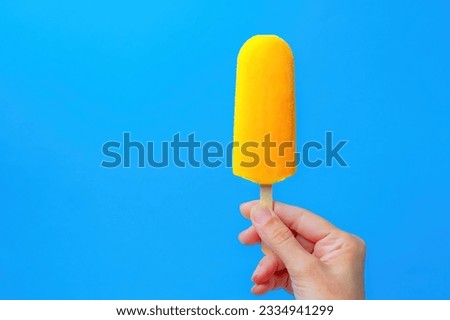 mango-flavored popsicle in a woman's hand on a blue background