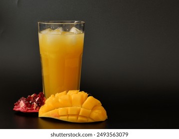 Mango-pomegranate juice in a tall glass with ice on a black background, next to ripe fruits. Close-up. - Powered by Shutterstock