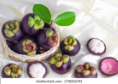 Mangosteen, fresh fruit placed alternately and mangosteen placed on a wooden basket Cut in half, showing white flesh inside With a thick purple shell, delicious flavor, satin background