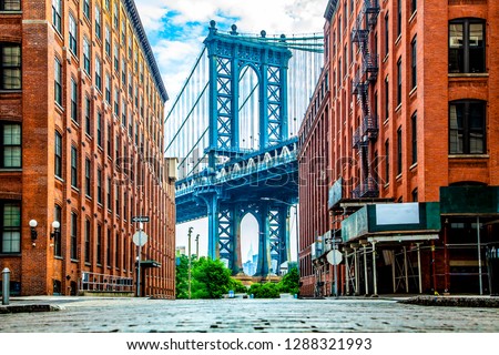Manhattan Bridge between Manhattan and Brooklyn over East River seen from a narrow alley enclosed by two brick buildings on a sunny day in Washington street in Dumbo, Brooklyn, NYC