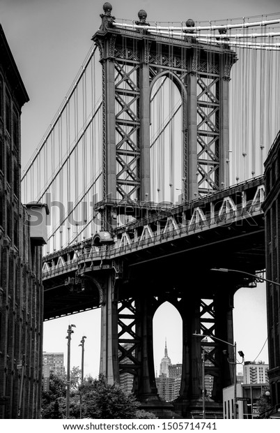 Manhattan Bridge in Brooklyn USA and skyscraper\
“Empire State Building“ underneath in the background. Steel\
construction connecting downtown New York with boroughs for cars,\
pedestrians and\
subway.