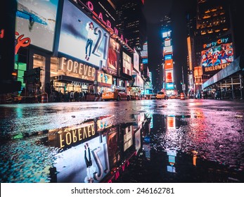 Manhattan, Circa Oct 2014: Typical Time Square Night View Scenery In New York City. Taxi, Lights And Tourist Are Reflected In A  Water Puddle