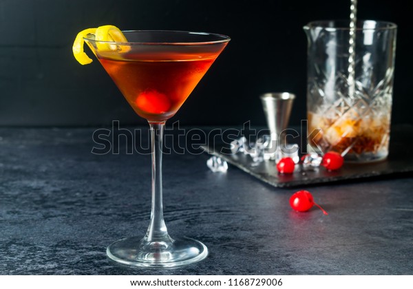 Manhattan Cocktail With Maraschino\
Cherry, Ice, Lemon Twist And Decanter On Dark\
Background