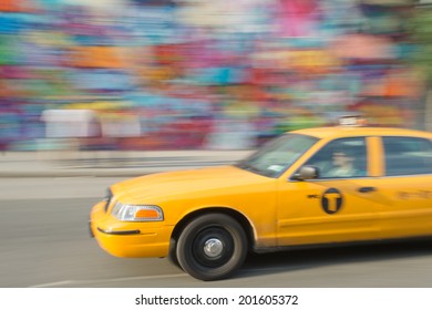 MANHATTAN, NY - JUNE 23: Fast taxi on the street and colorful graffiti painted wall in the background on June 23, 2014 in New York, USA.