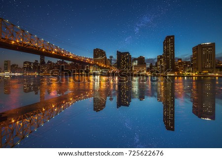 Manhattan panorama at dusk as seen from Roosevelt Island in New York, USA. New York night scene with East River waterfront illuminated buildings and starry sky with milkyway.