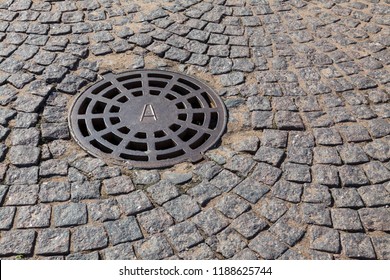 A manhole cover on a pavement of granite blocks