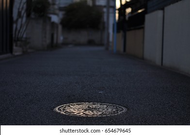 A manhole cover on the street and sunset in Tokyo residential area.