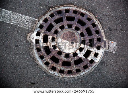 Manhole with metal cover in asphalt with white road marking line on it.
