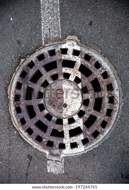 Manhole with metal cover in asphalt with white road\
marking line on it.
