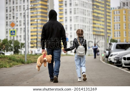 Maniac man holds the hand of teenage girl in street. The concept of kidnapping and child trafficking. Rear view on pedophile and caucasian child girl walking along the street. Crime, violence concept