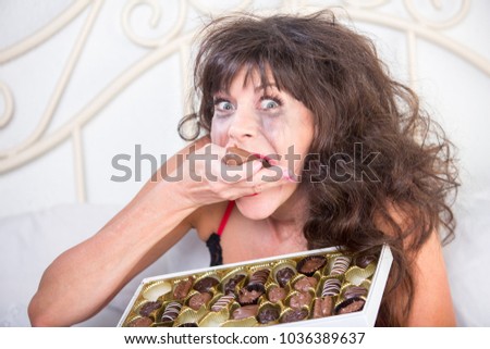 Manic mature woman crying and eating chocolates in her bedroom