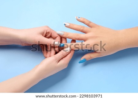 Manicure master applying press-on nail on blue background, closeup