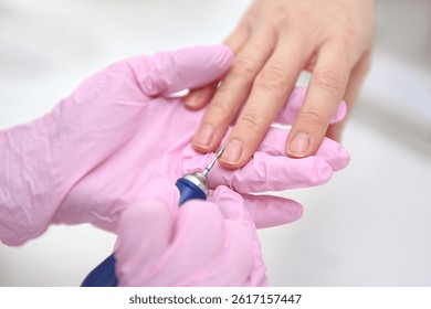 The manicure master performs a hardware manicure for the client in pink latex gloves, ensuring careful nail care so that they look flawless. Close-up of women's hands, hardware manicure