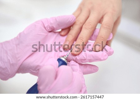 The manicure master performs a hardware manicure for the client in pink latex gloves, ensuring careful nail care so that they look flawless. Close-up of women's hands, hardware manicure