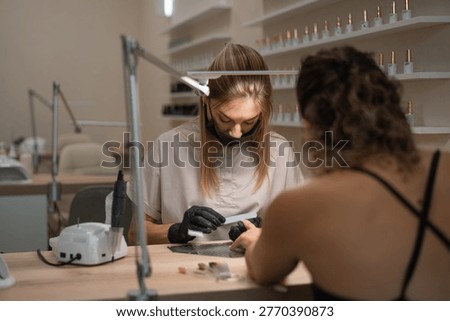 Manicure master sharpens nails with a file for a client at a table in a beauty salon