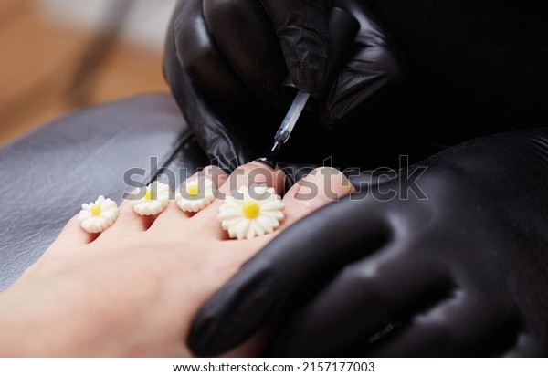 A manicure and pedicure master puts\
dividers on his fingers in a pedicure salon. Dividers for pedicure\
in the form of flowers. Black gloves on his hands.\
