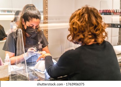 Manicure And Pedicure Salon, Coronavirus, Covid-19, Social Distance. The Reopening Due To The Pandemic, Security Measures. A Female Worker Behind The Protective Screen With Mask Trimmed Her Nails