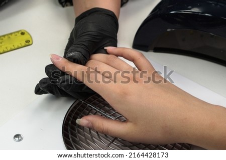 Manicure process. Cuticle cleansing, nail polish. Personal care, cosmetic procedure in the salon. Master's hands in black gloves.