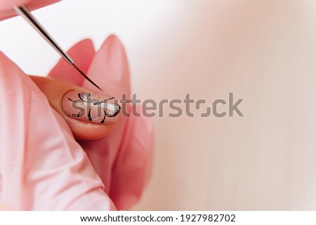 Manicure process. The master draws a butterfly drawing on the fingernail with a thin brush.