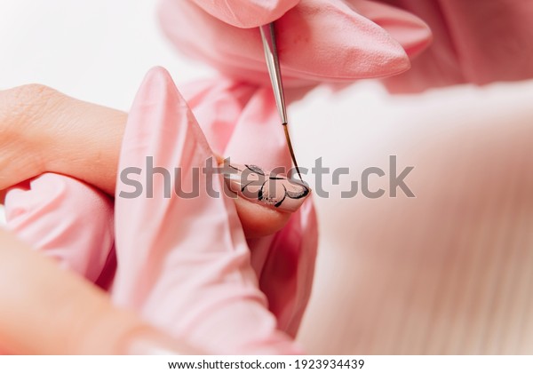 Manicure process. The master draws a\
butterfly drawing on the fingernail with a thin\
brush.