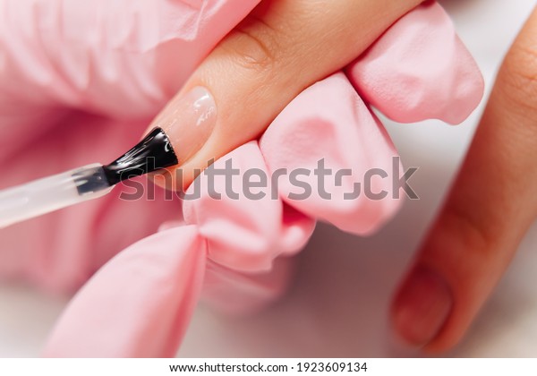 Manicure process. The master paints the nails\
with transparent\
varnish