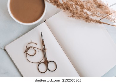 Manicure scissors with empty notebook and cup of coffee on table. Creative stylish workplace of manicurist. beauty treatment
