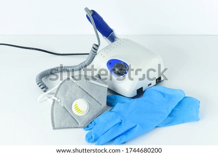 Manicure tools and equipment. A medical mask and rubber gloves lie next to the manicure machine.