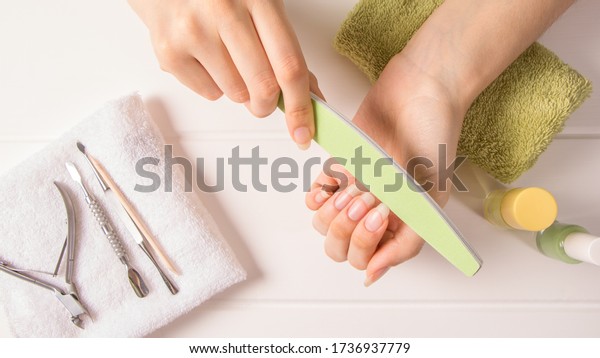 Manicure. A woman files her nails. Shorten long\
nails. Manicure tools. Home nail care, SPA, beauty. Long natural\
nails. Beauty salon.
