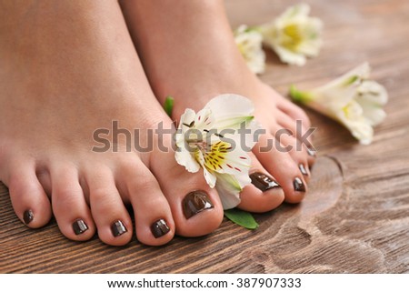 Manicured female feet with flowers on wooden background