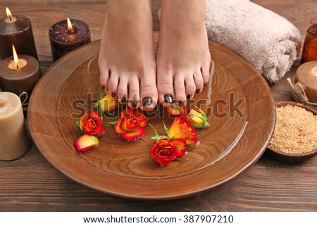 Manicured female feet in spa wooden bowl with flowers and water closeup