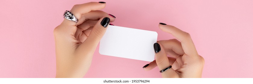Manicured womans hand holding postcard on pinkbackground