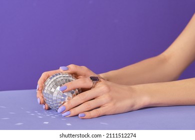 Manicured womans hands holding disco ball on violet background. Manicure, pedicure beauty salon concept