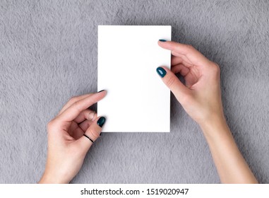 Manicured woman's hands holding postcard on grey furry background. Plain call-card mock up template.