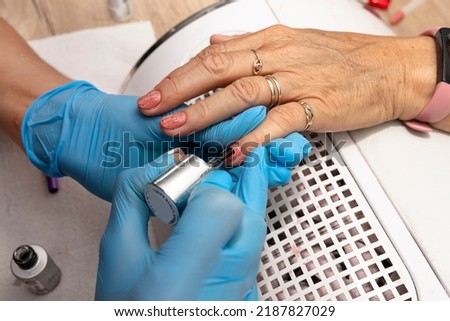 The manicurist applies a topcoat with black dots to the finished hybrid nails with a brush.