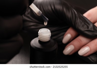 Manicurist In Black Gloves Paint The Girl's Nails With Varnish. Do A Manicure In The Salon, The Development Of Your Business. Close-up Of A Drop On A Brush