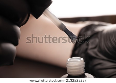 Manicurist in black gloves paint the girl's nails with varnish. Do a manicure in the salon, the development of your business. Close-up of a drop on a brush