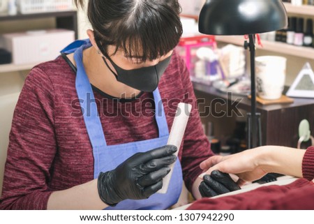 Manicurist in black latex gloves form the shape of a client's nail in a beauty salon.