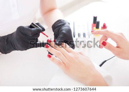 A manicurist in gloves paints a female nails with red lacquer. Beauty service, salon, health care and cosmetics. Close up.