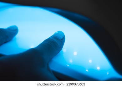 Manicurist Master Is Covering Painting Client's Nails Top Coat Shellac, Hands Closeup. One Hand Drying In UV Lamp. Professional Manicure With Gel Polish. Nail Art, Hands Care, Beauty Industry Concept.